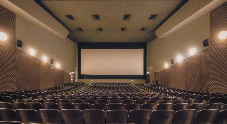 Una sala cinematografica vuota con diverse file di sedie e un grande schermo in fondo.